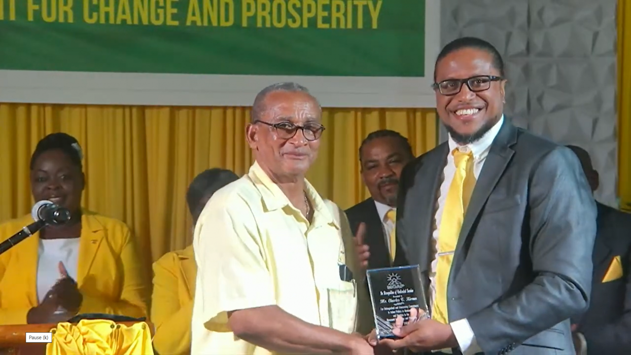 Minister Charles Kirnon is presented with an award for his service to MCAP and politics by party leader Dr Samuel Joseph. (screenshot)